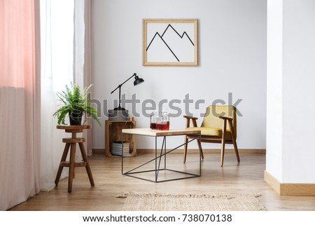 End table with three decanters with liquor, a mustard armchair and a picture on the wall above