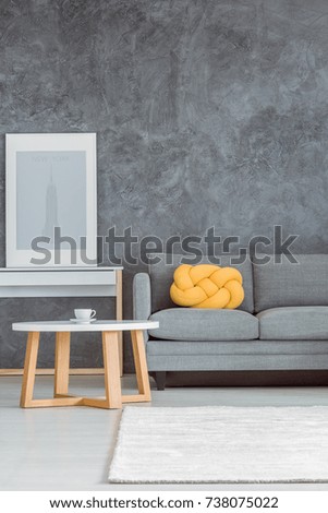 Simple beautiful living room with gray wall, comfortable couch, white and wooden coffee table, console table, poster, rug and yellow decorative pillow