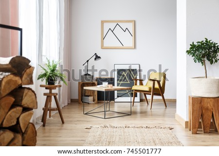 Apartment corner with pictures, end table, plants, wood, and a mustard armchair