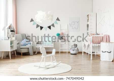 Stylish furniture in a monochromatic spacious kid's room with tulle pompons as decoration