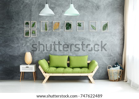 Set of framed tropical leaves and pastel lamps hanging above green wooden sofa, white cupboard and wicker basket with pillows