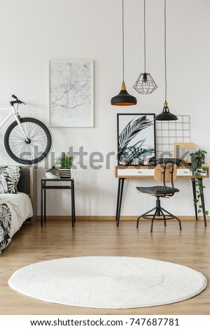 White round carpet in teenager\'s room with lamps above chair at desk and bike on bedhead