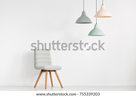 Grey chair against white wall with copy space in empty room with peach, mint and grey lamp