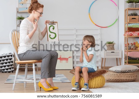 Cute little child with speech impediment and smiling young preschool teacher learning the alphabet letters in kindergarten classroom