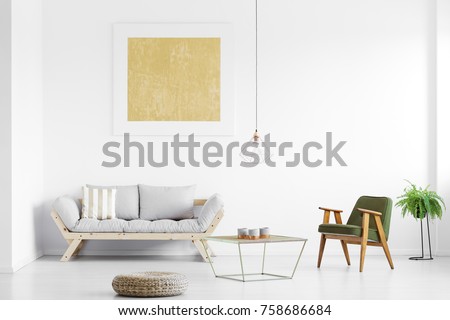 Gold painting above grey sofa in bright living room with armchair at table, pouf and fern