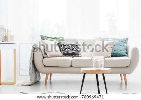 Candle in a glass jar on table in front of beige sofa with pillows in scandinavian style living room