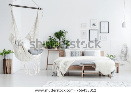 Hammock hanging in bright bedroom with potted plants, woolen coverlet on the bed and posters on white wall