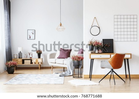 Round plate on the wall and designer chair at desk with heathers in bright living room interior with workspace