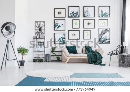 Blue carpet in bright living room with metal lamp and green blanket on sofa against wall with posters