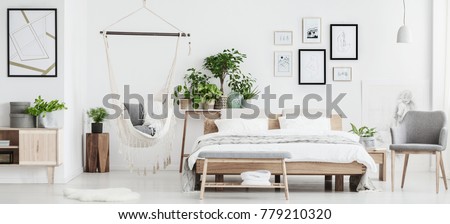 Plant on cupboard in spacious bedroom interior with hammock, gallery of posters and wooden furniture