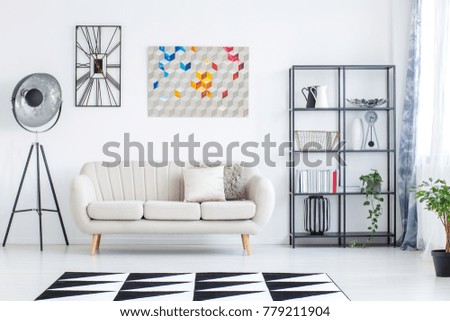 Bright living room interior with beige sofa, geometric carpet and oversize lamp standing against white wall