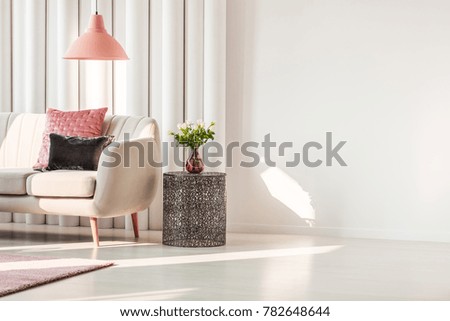 Simple living room interior with pink and gray cushions on beige sofa and roses on metal table