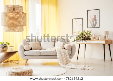 Oversize lamp in light living room with yellow drapes, beige sofa and knit blanket