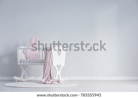 Pink blanket and pillow in white cradle against a wall with copy space in white baby's bedroom interior with rug