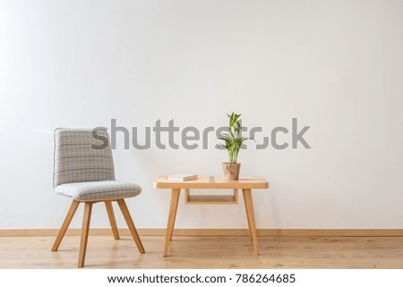 Grey comfy chair standing next to a small table with a book and a plant on it in a day room interior