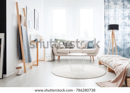 Minimalistic boho bedroom interior with a beige mattress lying on a wooden pallet and bright sofa