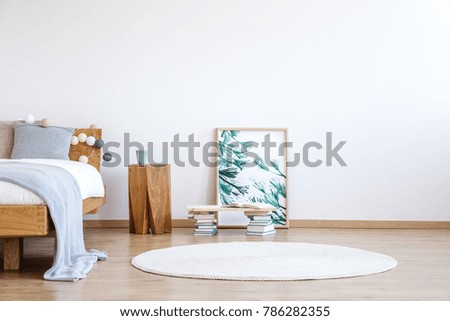 White round rug, books and floral poster on the floor next to a wooden stool and bed in bright bedroom