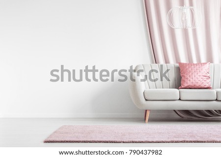 Pink rug in front of white sofa with satin pillow in bright living room interior with empty wall