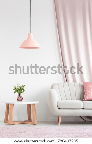 Bright living room interior with beige sofa, peach lamp, wooden table and roses in pink vase