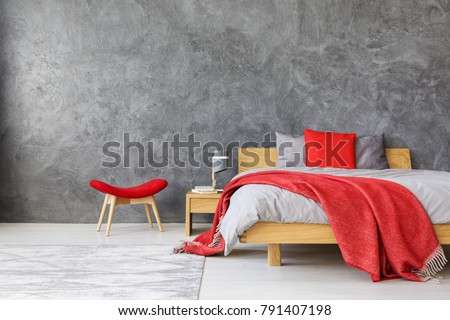 Grey spacious bedroom interior with king size bed with red color accents of blanket, pillow and stool
