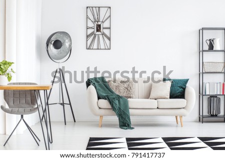 Dark green blanket on cream sofa and black lamp in modern living room interior