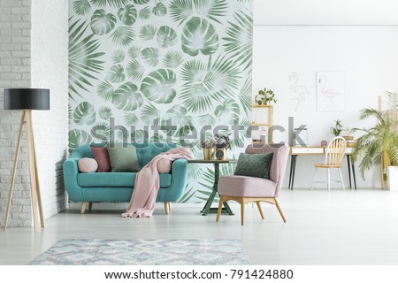 Turquoise lounge with pink blanket and pillows standing in stylish apartment interior with floral wallpaper