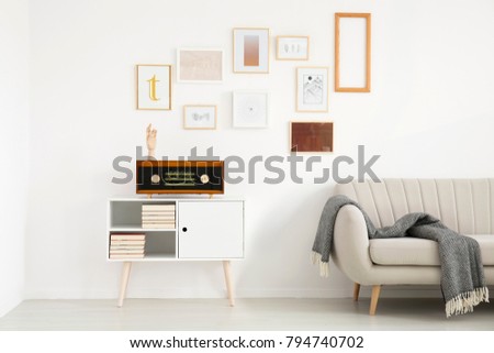 Blanket on beige sofa next to white cupboard with radio against the wall with mockup of poster in simple living room interior