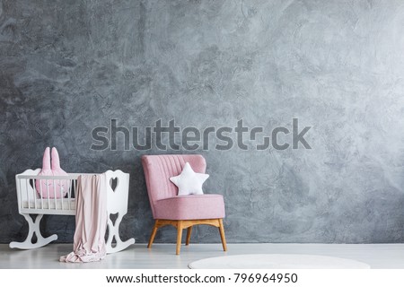 Simple bedroom interior for a newborn with pink armchair next to a white, wooden cradle
