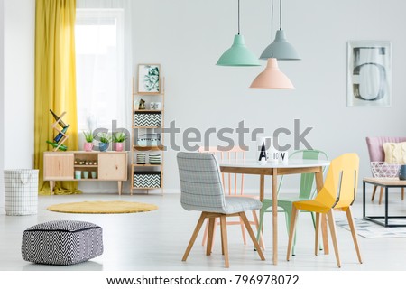 Feminine dining room interior with colorful chairs at the round table and wooden cupboard near the window with yellow drapes
