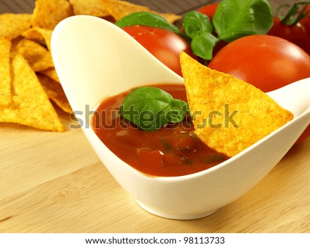 Mexican salsa sauce with nachos and tomatoes in a background.