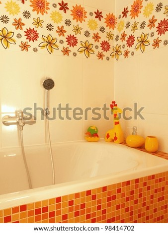 Closeup of a mosaic bath with a shower, yellow children toys and flower tiles