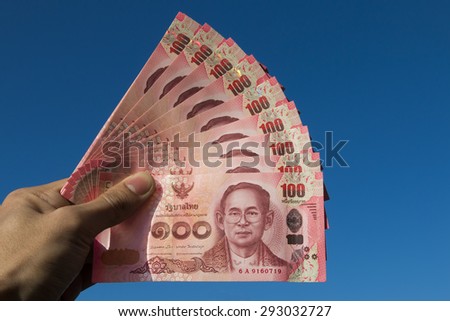 Asian men left hand hold few hundred banknotes of Thailand on the sky background (Thai baht)