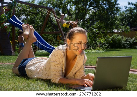 young beautiful mother works as a freelancer at home, on the green lawn in your garden, through the Internet, While her children play nearby.