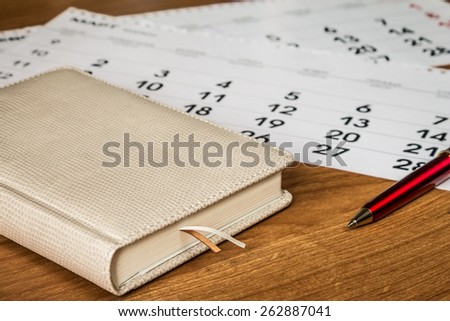 book laying on a wooden table, calendar, ball pen