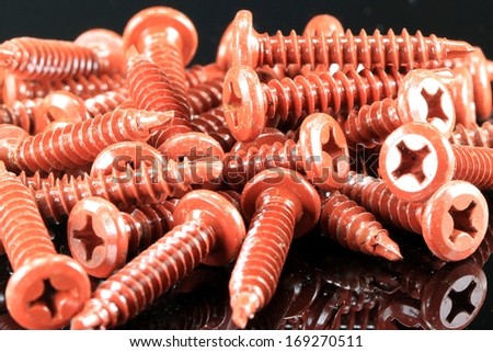 Pile of red metal construction screws on black background
