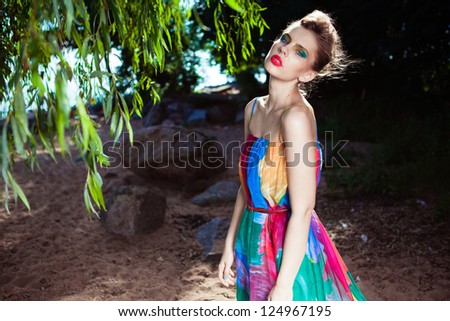 Young model posing in a bright dress on a beach near the deciduous tree
