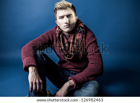 Stylish man in a sweater, jeans and a scarf on a blue background