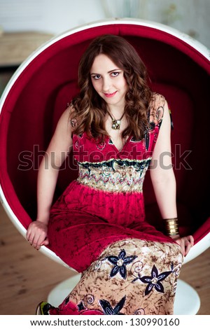 Smiling glamorous girl in a light dress sitting in a chair ball