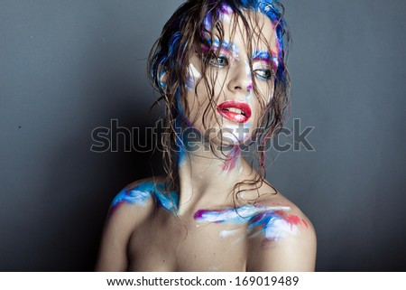 Creative art makeup of a young girl with blue eyes. Strokes of paint on his face and hair. Wet hair on her face
