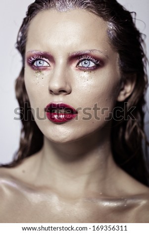 Cute young girl with creative make-up art. Glitter on her face, monochrome eyelashes, wet hair and fuchsia lips