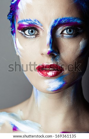 Creative art makeup of a young girl with blue eyes. Strokes of paint on her face and hair