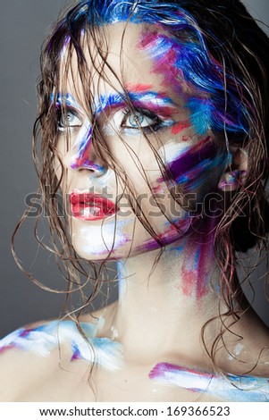 Creative art makeup of a young girl with blue eyes. Strokes of paint on her face and hair. Wet hair on her face