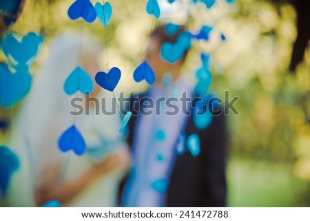 Blue heart in the foreground. High key blurred image of the couple. Unrecognizable faces, bleached effect.