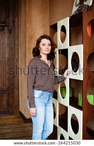 Middle-aged woman in jeans and a blouse standing near shelves