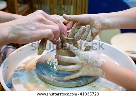 Adult and child attaches a handle to a clay bowl on a potter\'s wheel