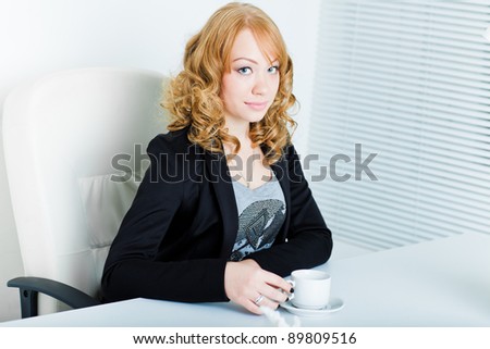 Young business woman sitting at work desk with coffee and flower