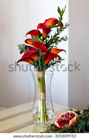 Bouquet of red calla lilies in a glass vase with a pomegranate on a white background