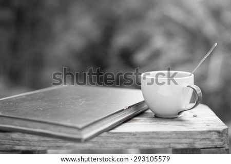 Coffee cup with a spoon and an old  book. Put on an old wooden table. in black and white tone With blur  background black and white from a tree soft.