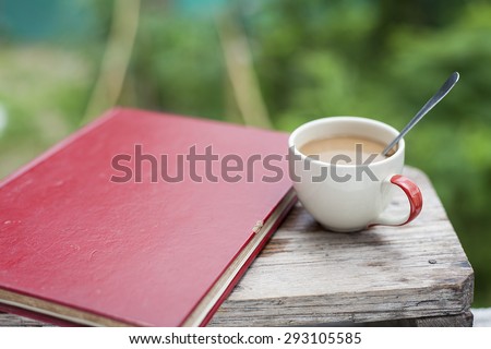 Coffee cup with a spoon and an old red book. Put on an old wooden table. With green background from a tree soft.