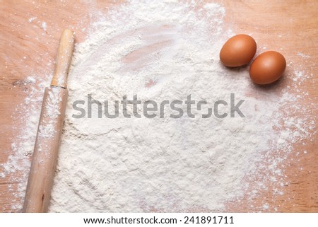 rolling pin and flour on the wooden board with eggs on it